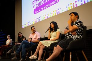 5 personas sentadas, una de ellas con un micrófono en la mano hablando