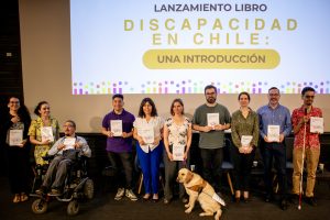 Grupo de personas de pie mirando a la cámara. Cada una tiene el mismo libro en la mano